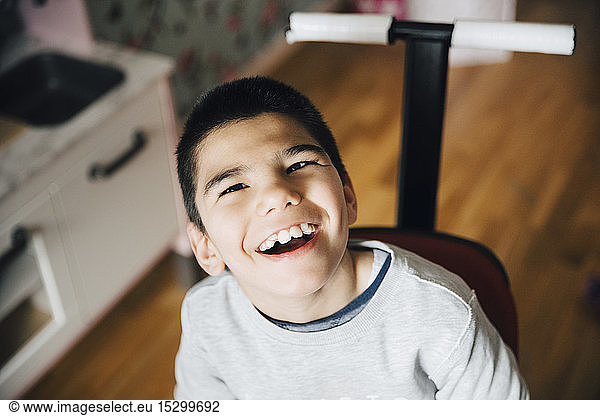 High angle view of happy disabled boy sitting on wheelchair at home