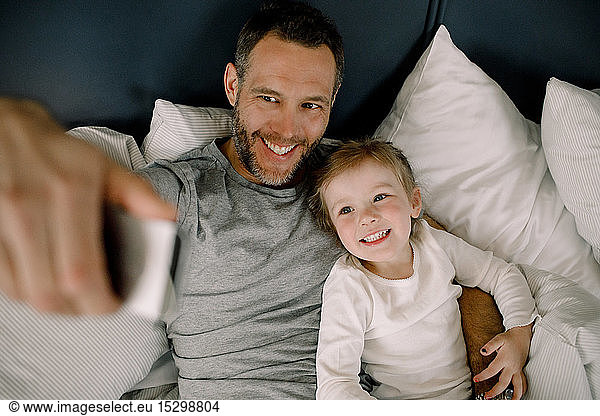 High angle view of happy father taking selfie with smiling daughter on bed in hotel