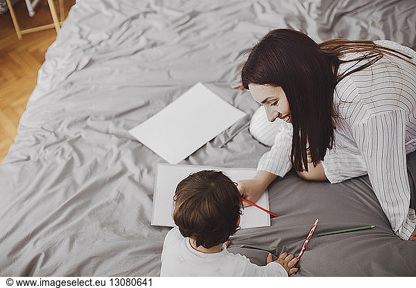 High angle view of happy mother and baby boy with school supplies on bed at home