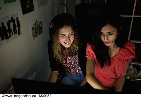 High angle view of happy teenage girl using computer with friend in darkroom at home