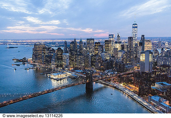 High angle view of illuminated Brooklyn Bridge over East River by cityscape at dusk