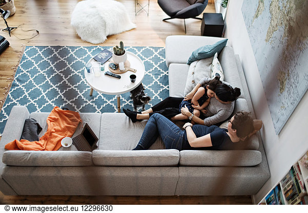 High angle view of lesbian couple talking with daughter while sitting on sofa by dog in living room at home