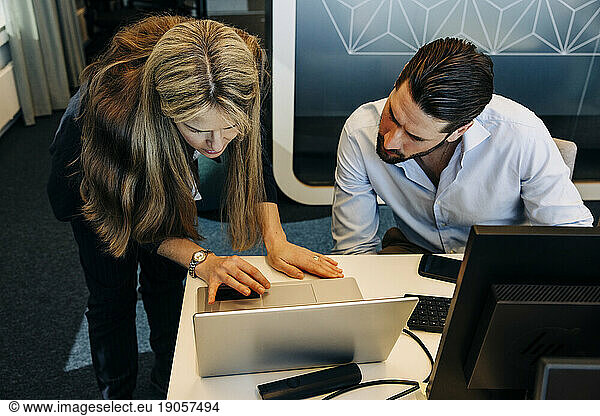 High angle view of male and female business colleagues working over laptop in coworking office