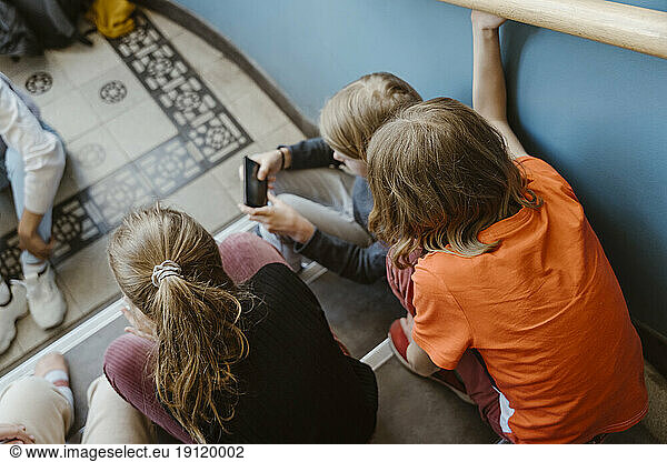 High angle view of male and female friends sitting on staircase of school building