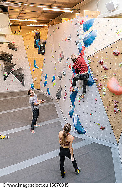 High angle view of male and female students looking at mature coach climbing wall in gym