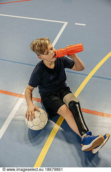 High angle view of male athlete drinking water after football match at sports court