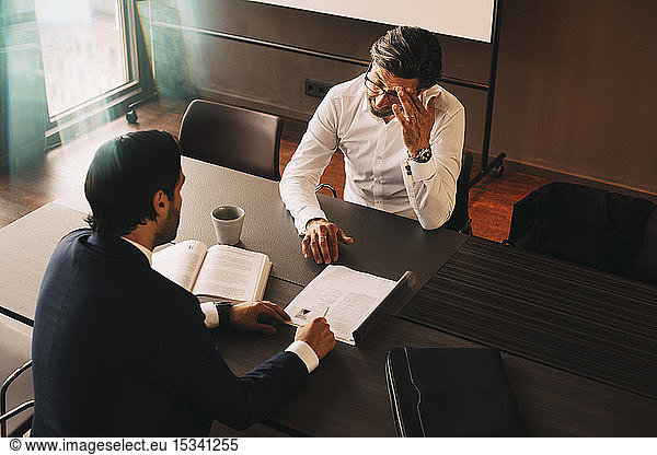 High angle view of male lawyer showing file to mature stressed client at board room in law office