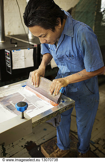 High angle view of man pressing ink on frame in workshop