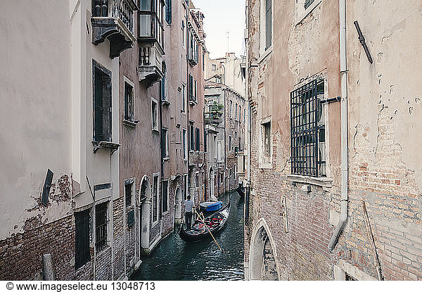 High angle view of man standing in gondola on canal amidst residential buildings in city