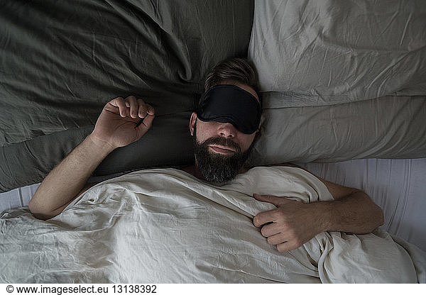 High angle view of man wearing sleep mask while sleeping on bed at home