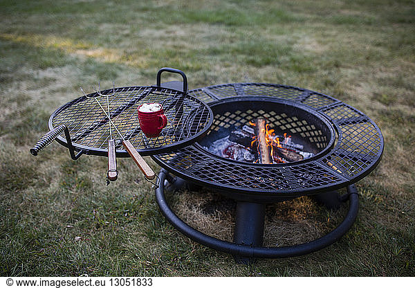 High angle view of marshmallow in mug and skewers on barbecue grill at yard