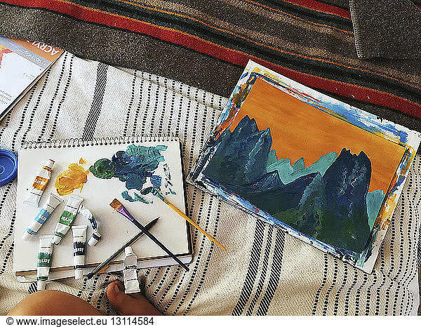 High angle view of paintings with paint tubes and paintbrushes on bed in motor home