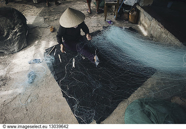 High angle view of person in conical hat repairing fishing net
