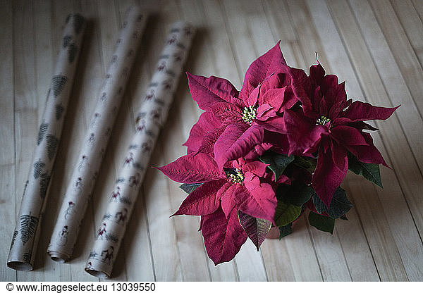 High angle view of poinsettia by wrapping papers on wooden table