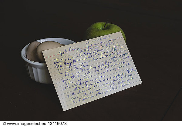 High angle view of recipe with eggs and granny smith apple over black background
