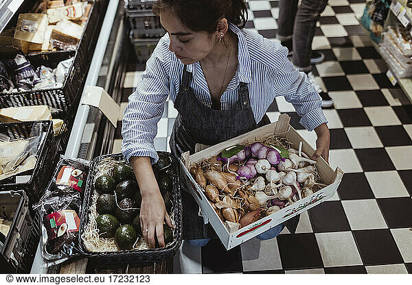 High angle view of sales woman arranging fruits and vegetables in box at deli store
