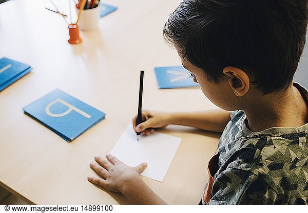 High angle view of schoolboy practicing alphabets at table in classroom