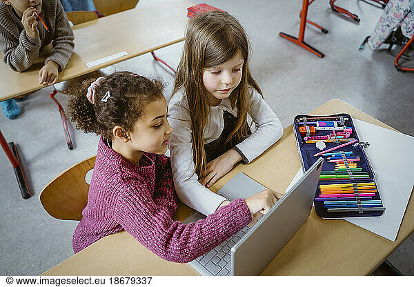 High angle view of schoolgirls using laptop together at desk in classroom
