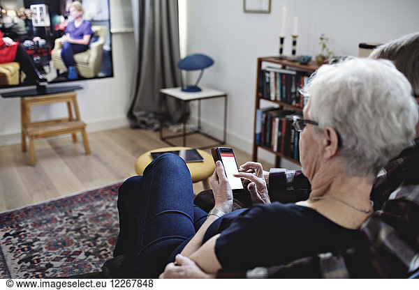 High angle view of senior couple sitting with smart phone watching TV at home