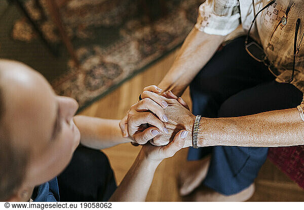 High angle view of senior woman holding hands of female caregiver at home