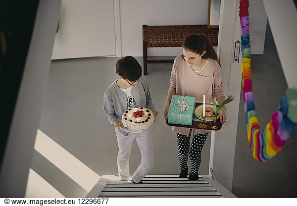 High angle view of siblings carrying birthday cake and gift box while climbing up steps at home