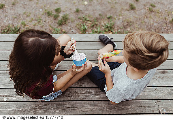 High angle view of siblings eating sweet food while sitting on wooden steps
