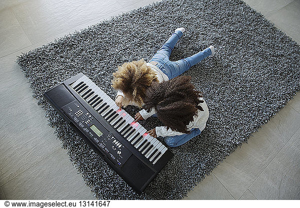 High angle view of sisters playing keyboard instrument on carpet at home