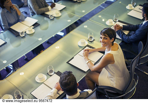High angle view of smiling businesswoman looking at camera and sitting in conference room