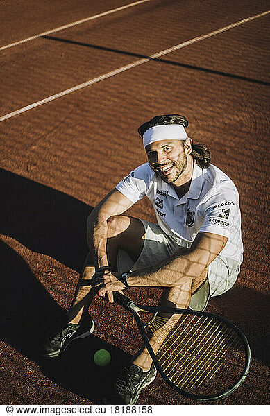 High angle view of smiling man with tennis racket sitting on ground during break