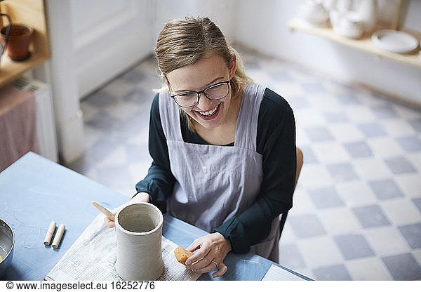 High angle view of smiling woman learning pottery in art class