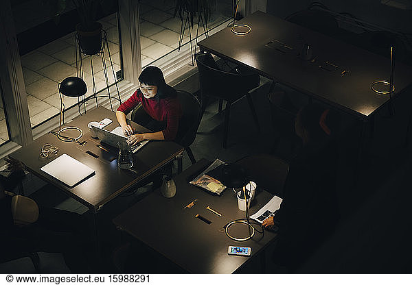 High angle view of smiling young businesswoman working late while using laptop at desk in coworking space