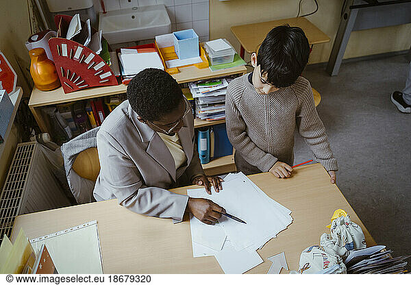 High angle view of teacher helping boy with diagram at desk in classroom