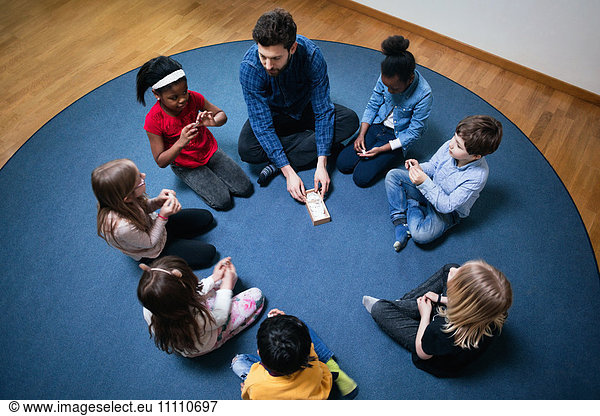 High angle view of teacher playing with children on floor at school