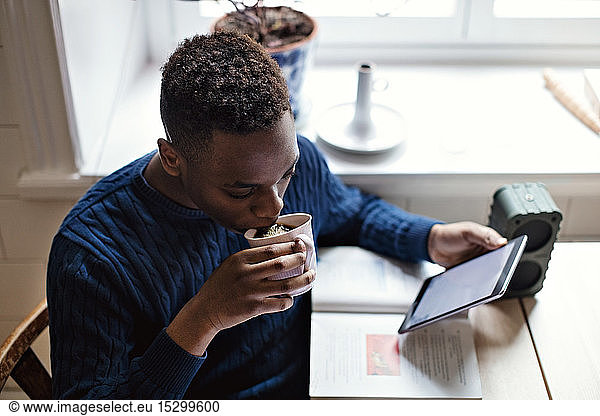 High angle view of teenage boy drinking black coffee while E-learning using digital tablet at home