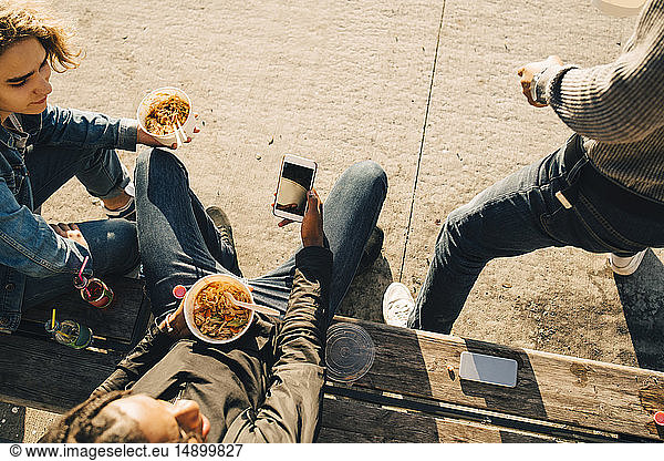 High angle view of teenage boy using smart phone while eating meal with friends on street in city