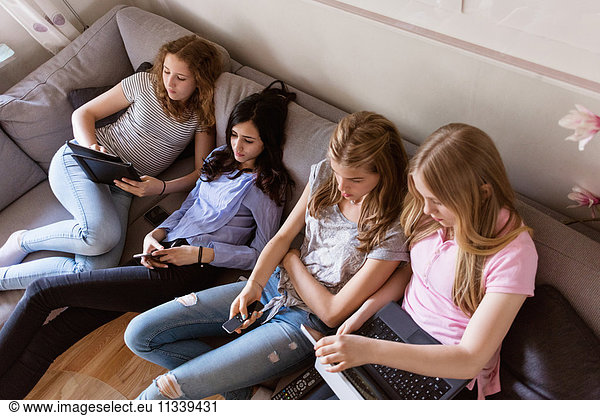 High angle view of teenage girls using technologies while watching TV in living room
