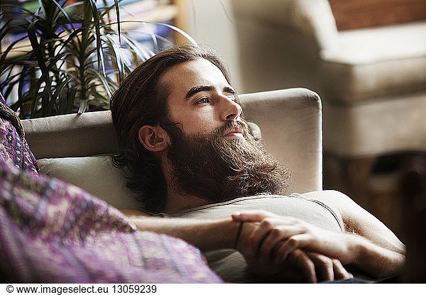 High angle view of thoughtful man relaxing on sofa