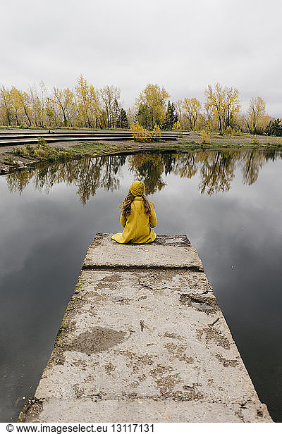High angle view of thoughtful woman sitting on pier over lake