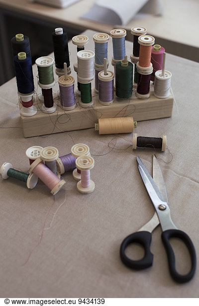 High angle view of various thread spools and scissors on table