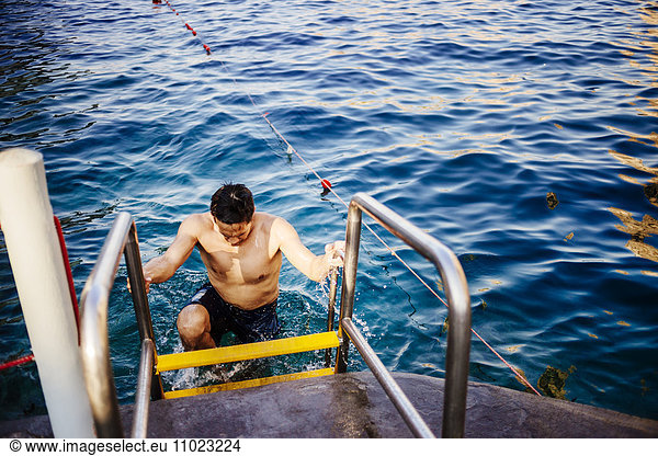 High angle view of wet man climbing ladder at shore