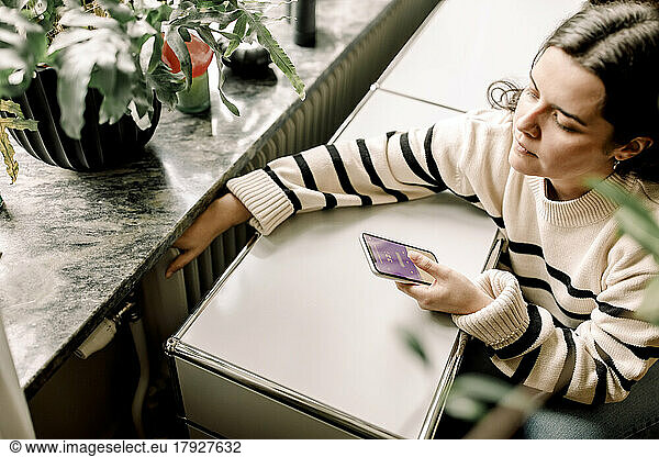 High angle view of woman checking temperature of radiator through smart phone application at home