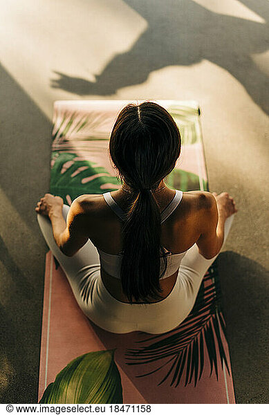 High angle view of woman meditating while sitting on exercise mat