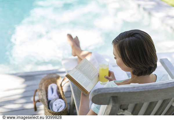 High angle view of woman reading and drinking juice by swimming pool