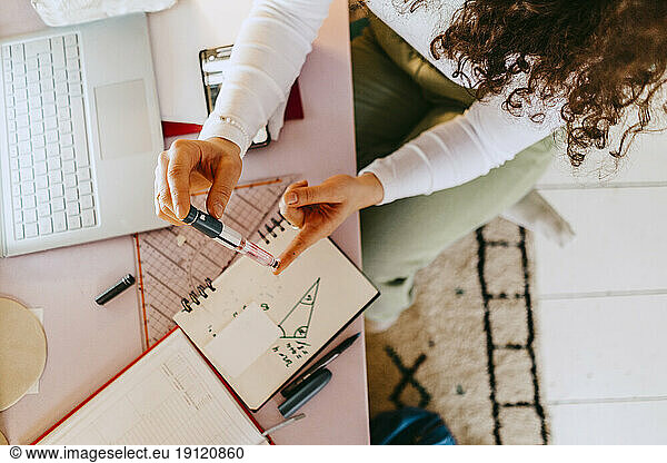 High angle view of woman using glucometer while doing homework at table