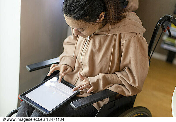 High angle view of woman with paraplegia using tablet PC while sitting on wheelchair at home