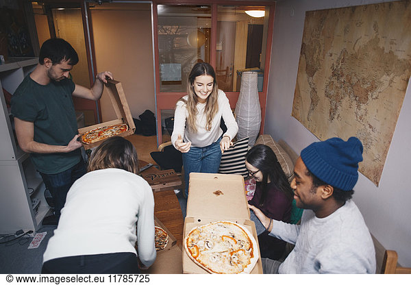 High angle view of young friends enjoying pizza party in dorm room