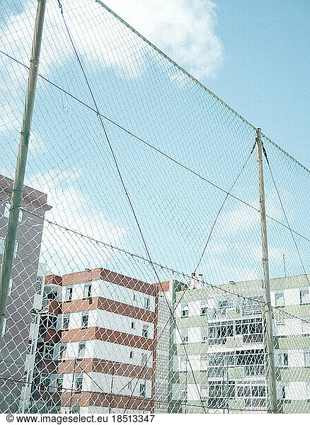 High ball stop fence on court against colorful buildings and blue sky