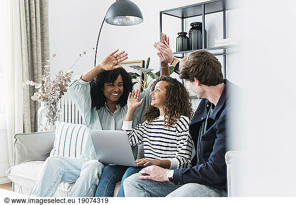High fiving happy parents sitting on sofa with daughter using laptop