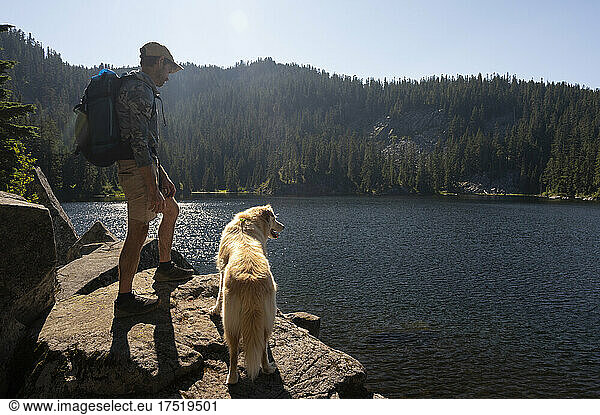 Hiker and dog standing next to an alpine lake
