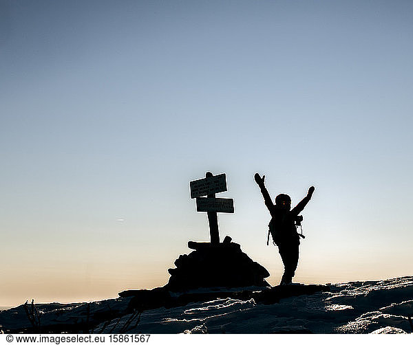 Hiker celebrate reaching summit with arms up on cold morning.